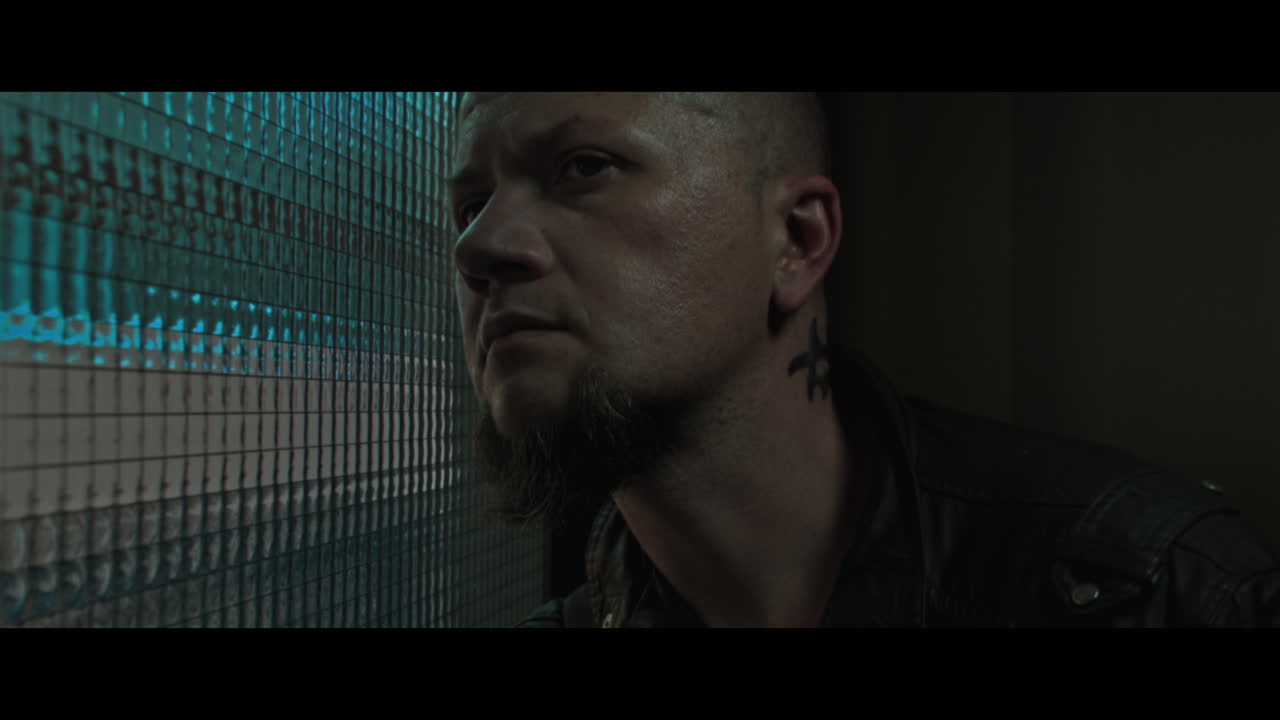 A bald dangerous looking man checks the corridor through reinforced glass