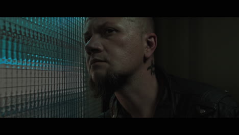 a bald dangerous looking man checks the corridor through reinforced glass