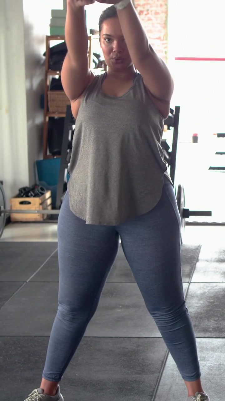 Video verticale: Donna con canotta grigia che afferra un kettlebell e si allena in una palestra in garage per la forza.