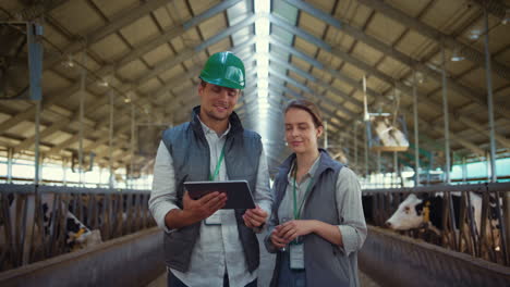 Livestock-workers-posing-cowshed-together.-Holstein-cows-eating-in-feedlots.