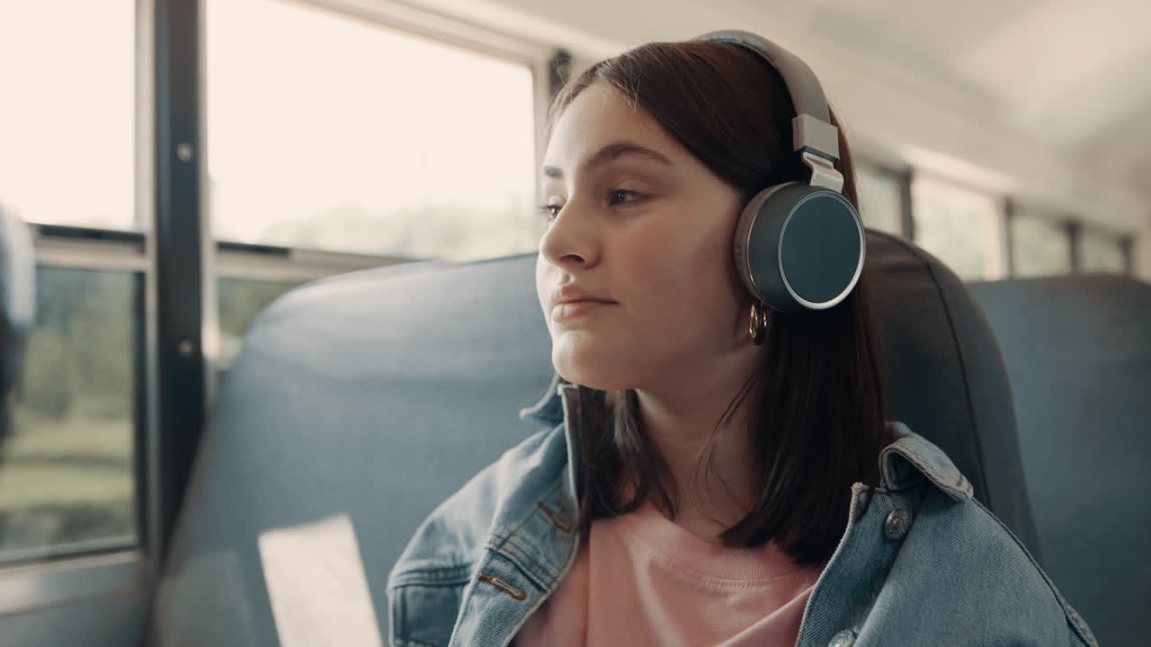 Ragazza adolescente che ascolta musica con le cuffie seduta sull'autobus, primo piano.