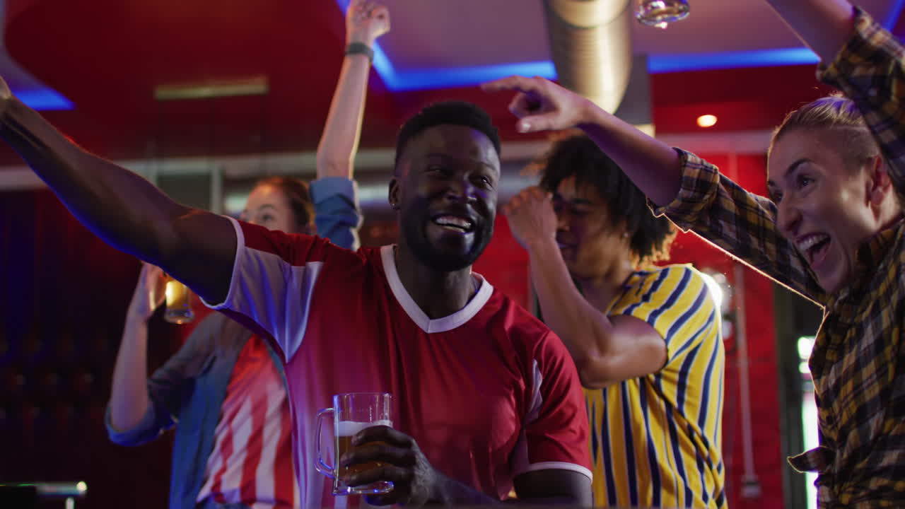 video de un grupo diverso de amigos felices bebiendo y viendo juegos deportivos en un bar, celebrando