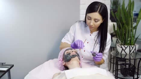 pretty cosmetologist with long hair makes a mask to a woman for cleansing the pores on the face in cosmetology. cosmetic procedures. spa