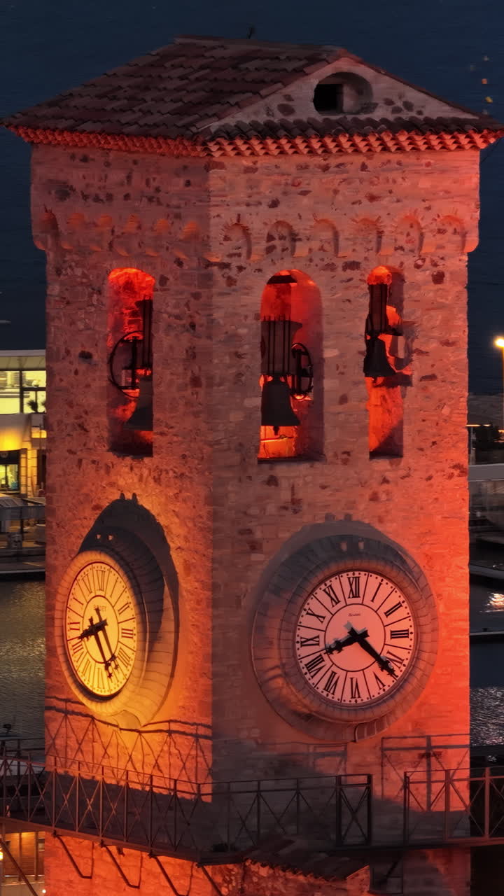 Aerial drone view of the historic Cannes clock tower at dusk, with the bustling city center in the background, glowing with evening lights. Vertical