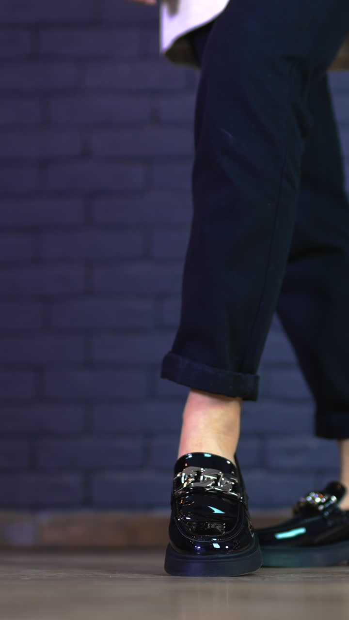 Girl in black jeans demonstrating modern massive shoes with silver chain decoration. Grey brick wall background. Vertical video