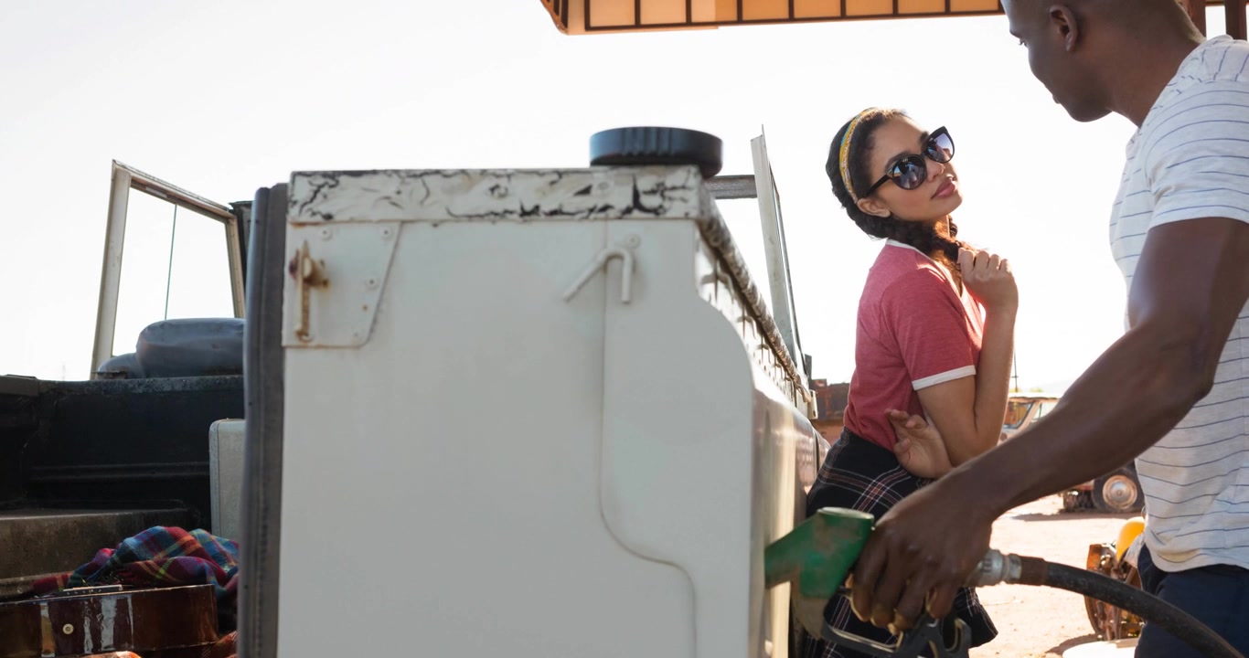 Diverse man and woman using fuel pump filling up truck at petrol station