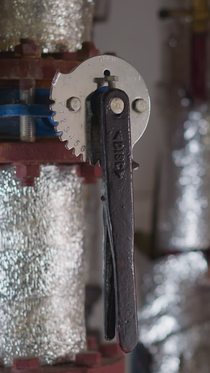 Metal fittings covered with silver foil insulation and levers in boiler premise closeup. Hot steam delivering pipeline system in mechanical room