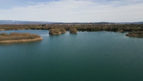 Drone-descends-above-shimmering-pond-water-with-tall-reed-islands-ancient-Antela-lagoon-Areeiras-da-Limia-in-Xinzo-de-Limia-Ourense-Galicia-Spain