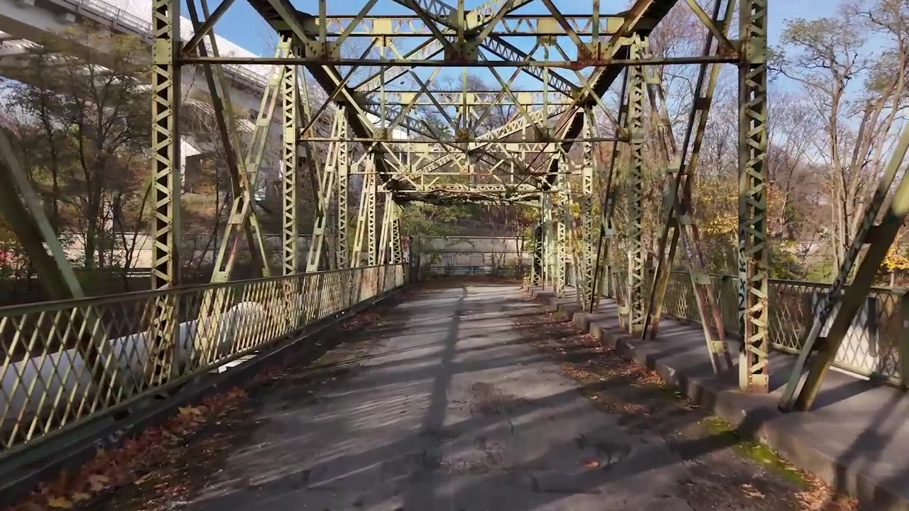 Volo con drone attraverso un vecchio ponte pedonale arrugginito, autostrada e traffico sullo sfondo.