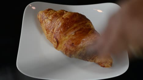 a croissant bread placed on a white plate using tongs - close up