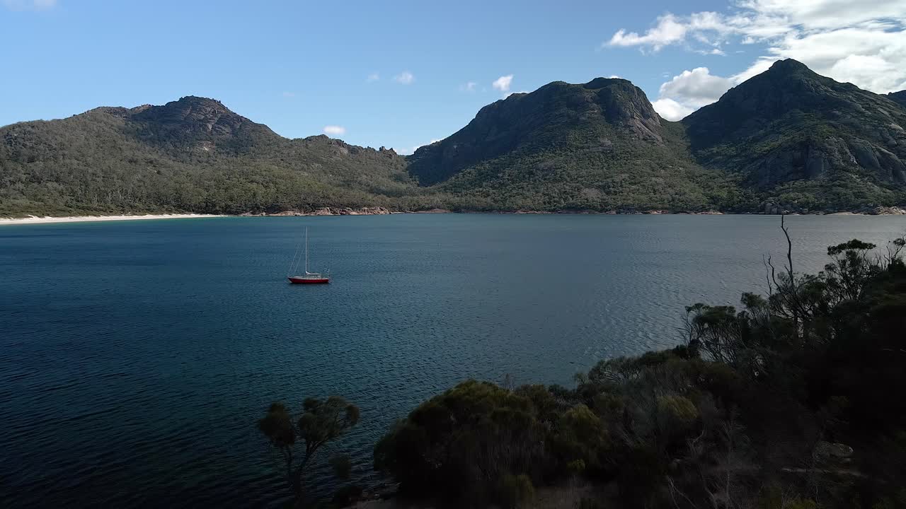 vista de perfil de las colinas del parque nacional de freycinet con un barco navegando en un lago en primer plano en tasmania, australia