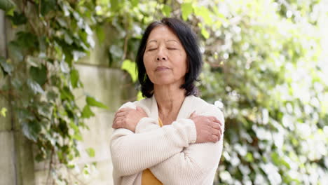 meditating peacefully, senior asian woman surrounded by lush greenery outdoors