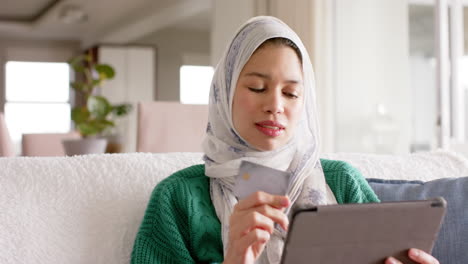 Biracial-Frau-Im-Hijab-Mit-Tablet-Auf-Dem-Sofa-Zu-Hause-Mit-Kopierplatz,-Zeitlupe