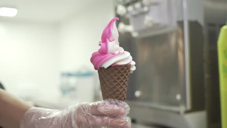 en mano con guante desechable con fresa de vainilla servido en un cono de helado