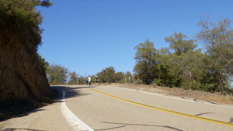 Three-men-carrying-skateboards-walking-up-Glendora-Mountain-Road-in-California-as-a-white-pickup-truck-drives-past-them