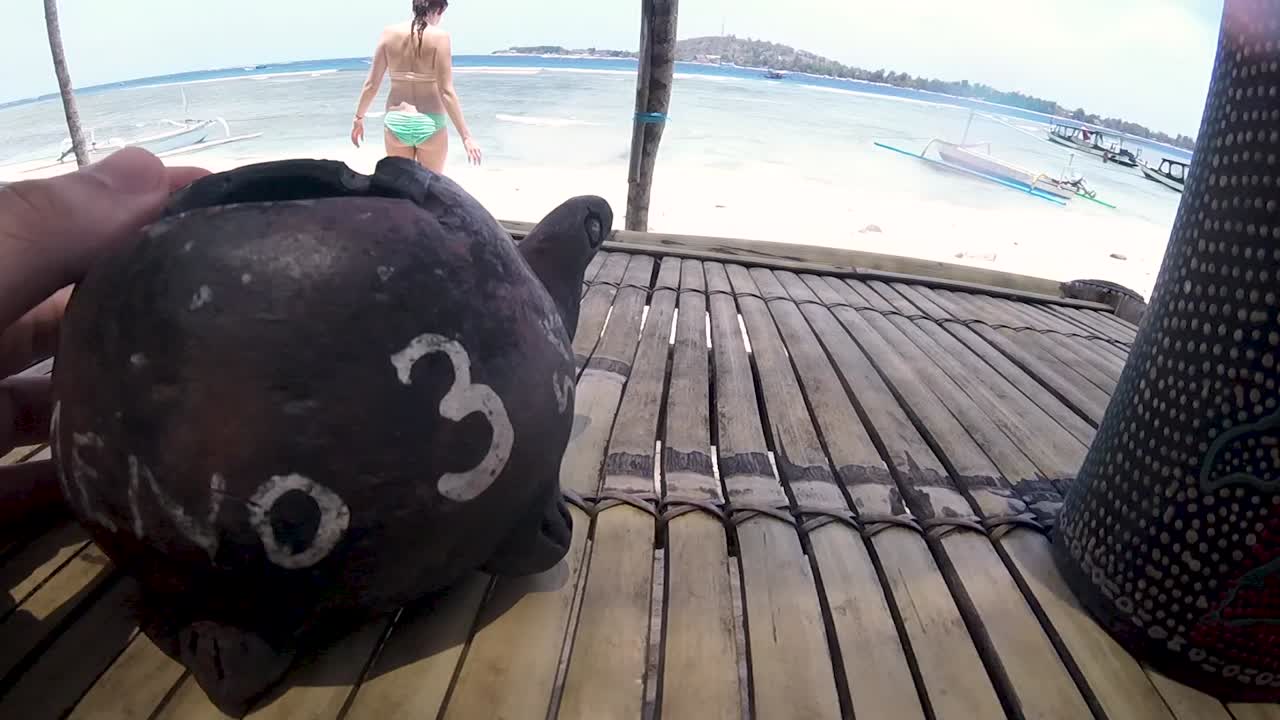 Wooden beach table with number in Gili Meno, Indonesia. Female with swimsuit enjoy sunny day on sandy coast