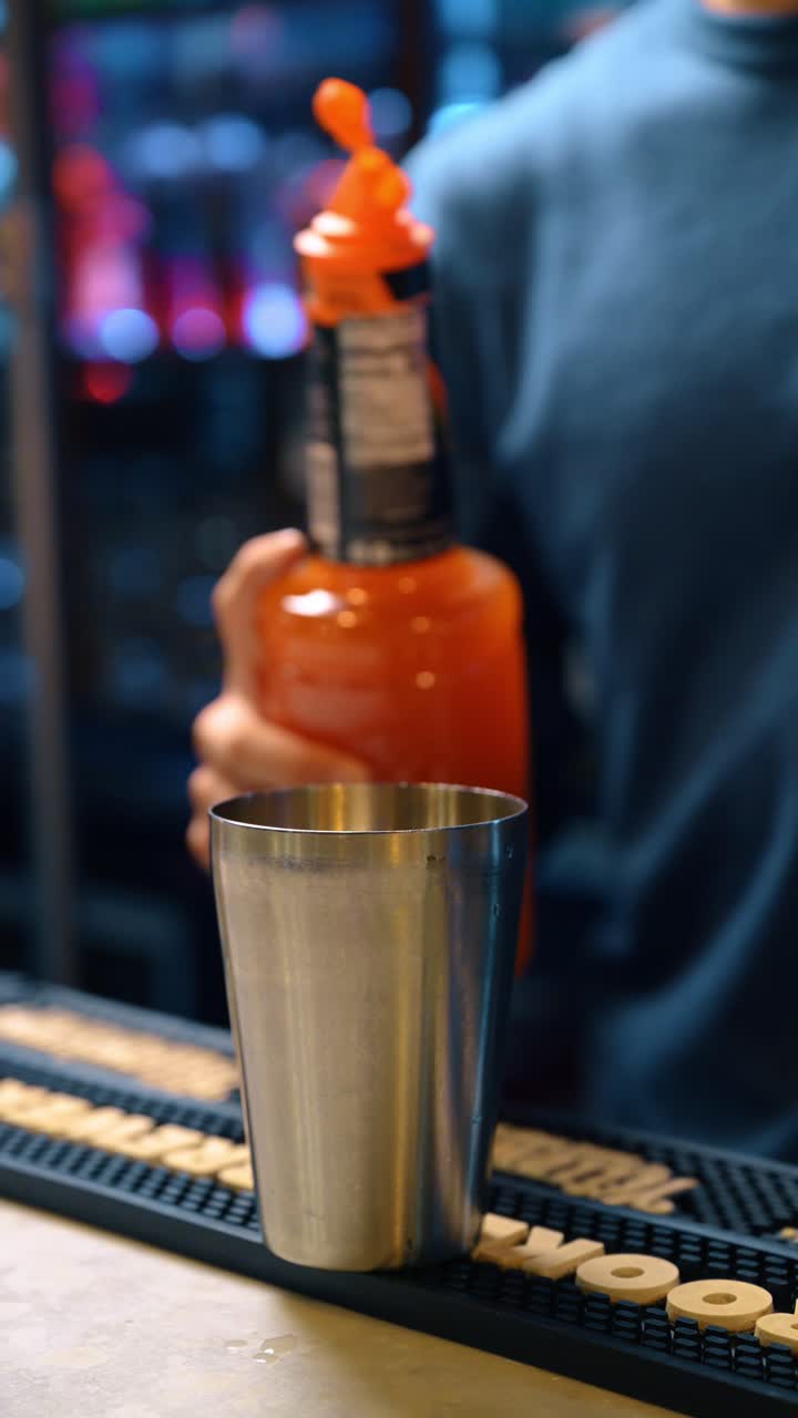 Barman che misura sciroppo d'arancia in un jigger per un cocktail artigianale. Versando liquido arancione brillante da una bottiglia per la mixology al bar