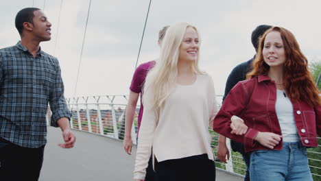 group of student friends walking across bridge in city together