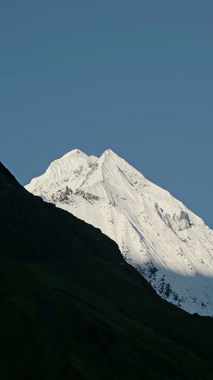 Primo piano verticale di cima montuosa innevata e cielo azzurro limpido, video verticale per social media Instagram Reels e TikTok delle montagne innevate dell'Himalaya, un popolare percorso per escursioni e trekking