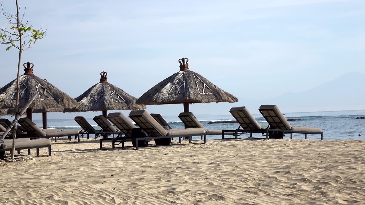 las olas del mar cálido corren en la playa de arena del complejo tropical con sombrillas y sillones