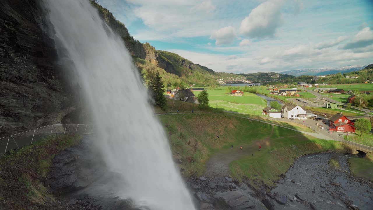 A famous Steinsdalsfossen waterfall in the village of Steine, Norway.  A mass of whitewater falling off the mountain in cascades. The valley with farms, houses, and roads stretches up to the horizon
