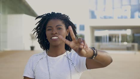 smiling young woman with dreadlocks showing peace signs.