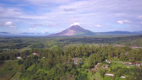 reverse drone shot of mount sinabung volcano and the surrounding beautiful green village in berastagi, north sumatera indonesia