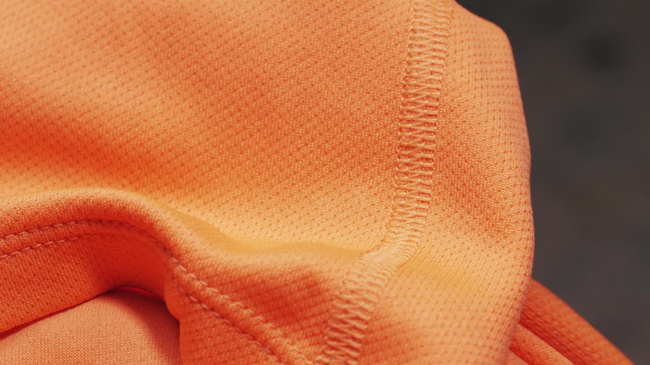 An orange polyester T-shirt shows mesh texture and a stitched seam as the camera pans slowly from left to right