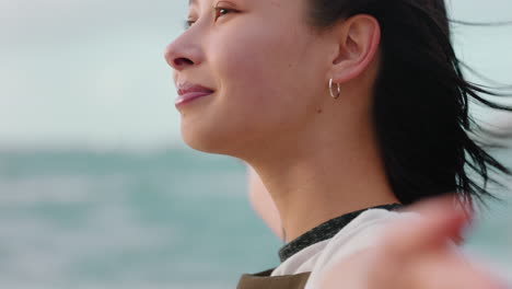 portrait of happy asian woman enjoying freedom arms raised feeling joy on beach at sunset exploring wanderlust with wind blowing hair