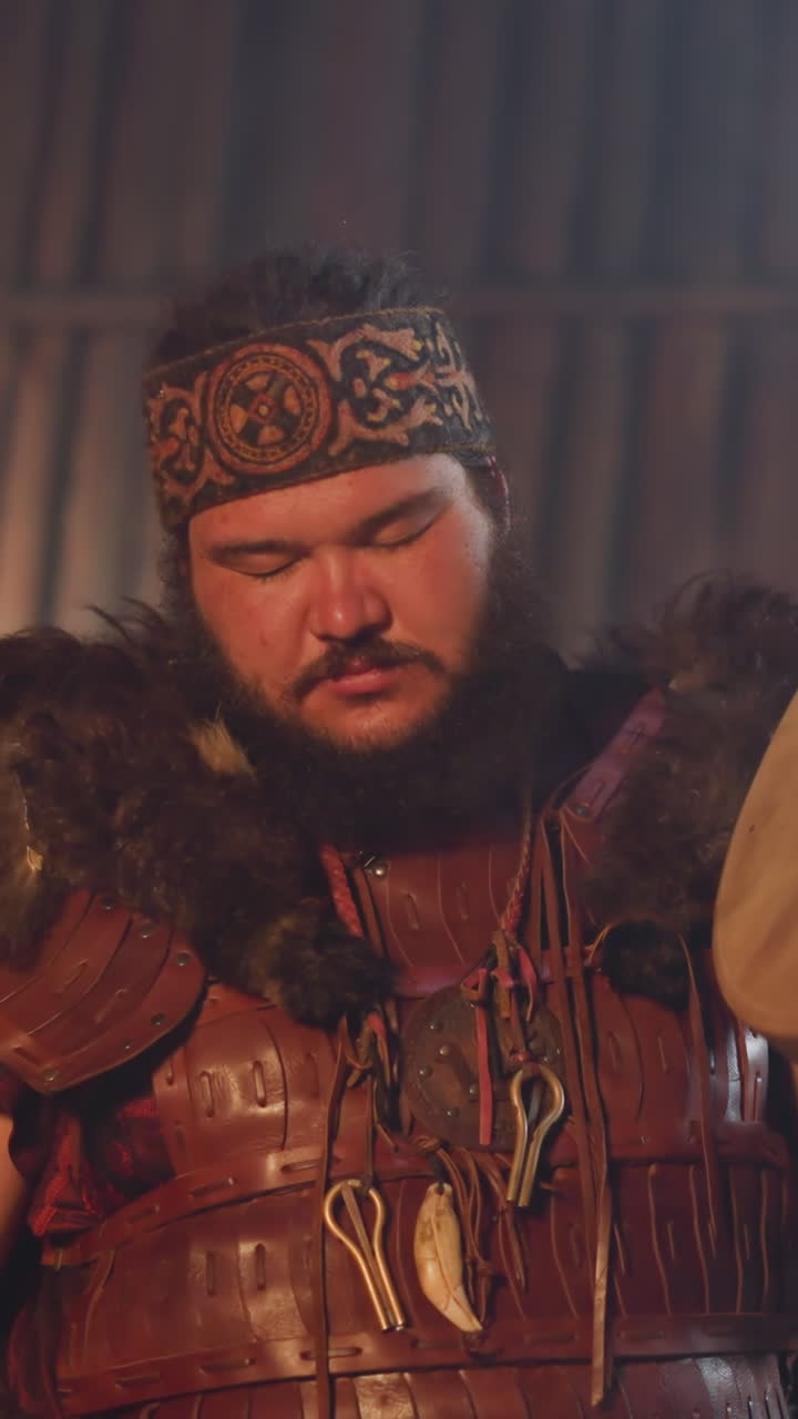 Man in spiritual ecstasy with closed eyes taps shamanic drum with special furry stick doing ritual closeup. Cosplayer in Altai national suit plays on stage