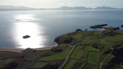 aerial view revering across lush ynys llanddwyn island with hazy snowdonia mountain range across sunrise shimmering irish sea