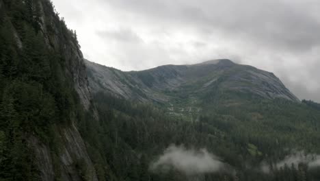 Eine-Neblige-Bergkette-In-Einem-Alaska-Fjord-Offenbart-Tiefe,-Felsen-Und-Vegetation,-Während-Die-Landschaft-Am-Himmel-Ruht