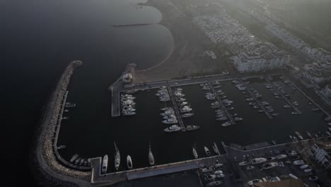 "drone footage at sunset over la duquesa port in sabinillas, málaga. a bird's-eye view advances over the marina, showcasing docked boats, the harbor, and the serene coastal charm."