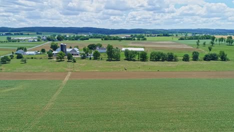 an aerial view of the farm countryside with planted fields and pastures a farmer working and a train passing by on a beautiful sunny day