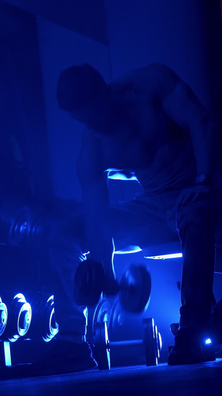 Bodybuilder in gym doing exercise. Fitness man bodybuilder with muscular torso workout with dumbbells in gym. Vertical video