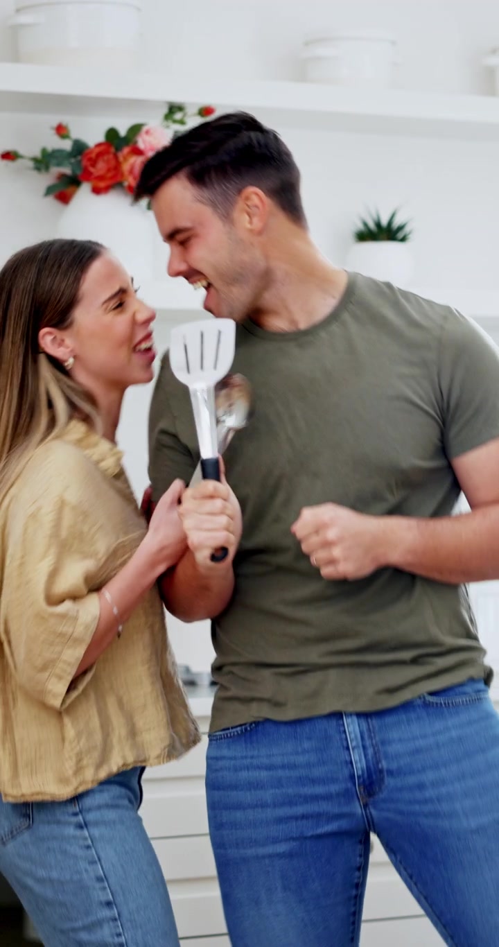 Coppia felice che canta e balla in cucina con utensili da cucina