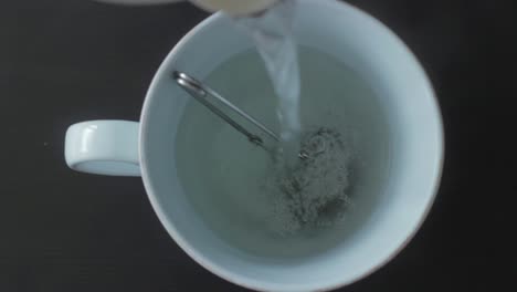 verter agua caliente en el colador de té con hierbas en la taza, vista de arriba hacia abajo