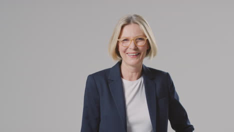 Retrato-De-Estudio-De-Una-Empresaria-Madura-Sonriente-Con-Gafas-Contra-Un-Fondo-Liso