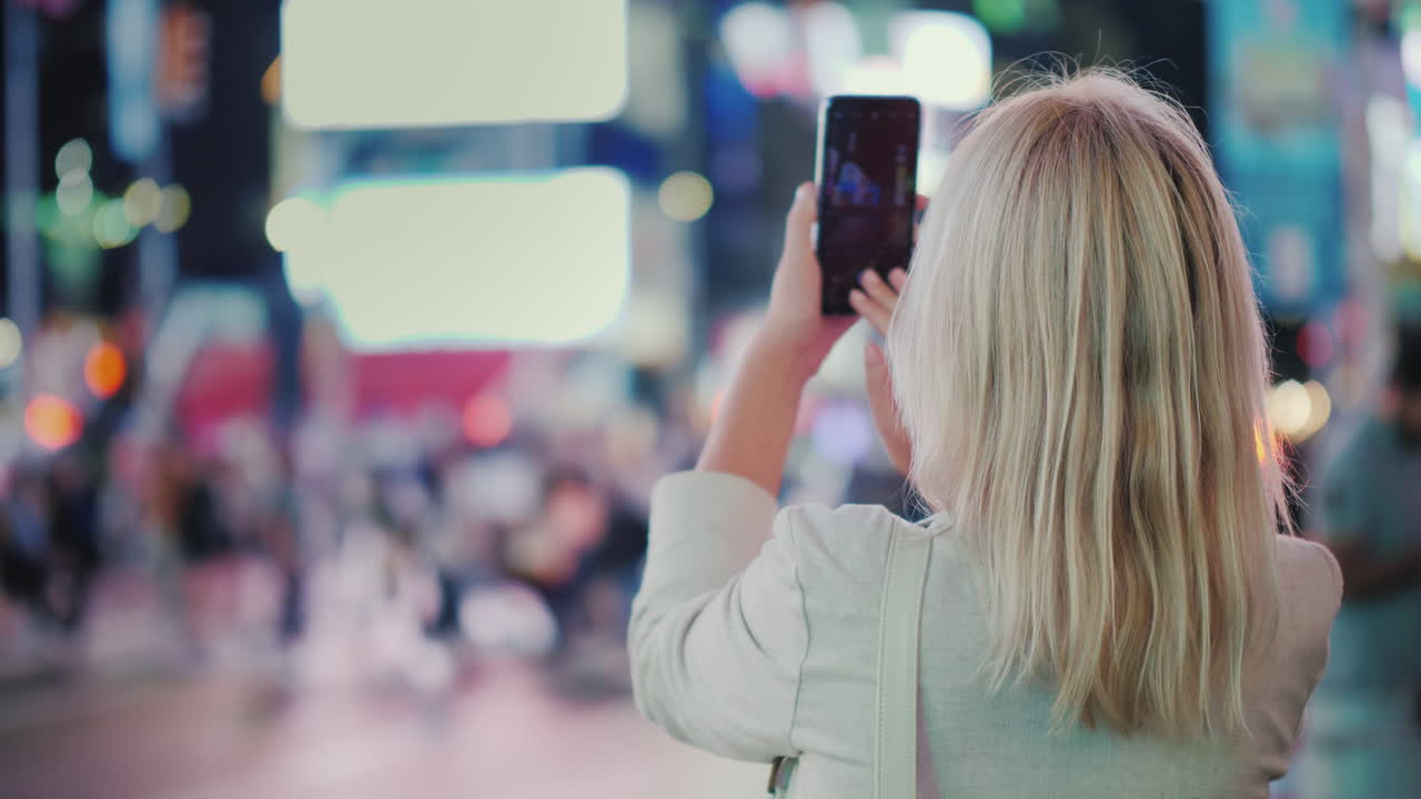 관광객은 뉴욕 후면의 유명한 타임스퀘어에서 스마트폰으로 사진을 찍습니다.