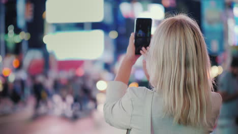 tourist takes pictures with a smartphone on the famous times square in new york rear view