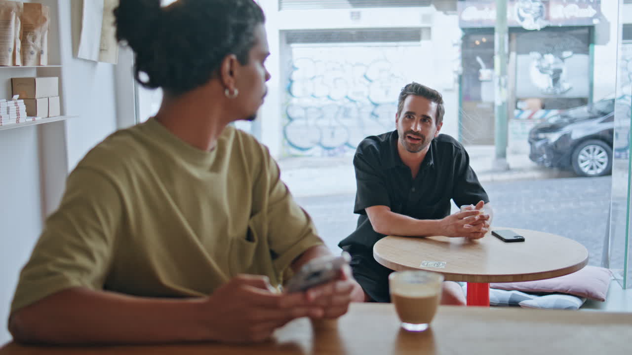 Two guys meeting cafeteria sitting morning. Man start talking to  hipster.