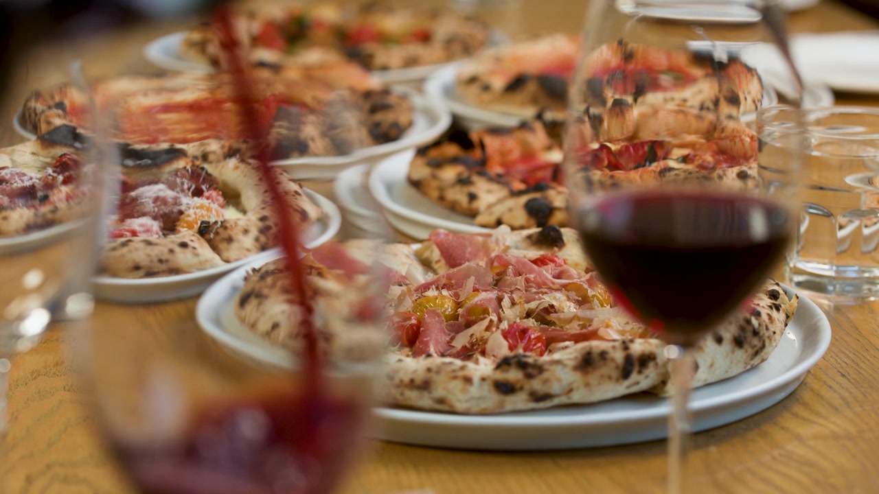 Vino rosso che si versa in un bicchiere su un tavolo di legno con pizze napoletane e prosciutto