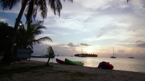 a static shot of three kayaks on the beach with boats floating on the ocean behind during sunset in san blas