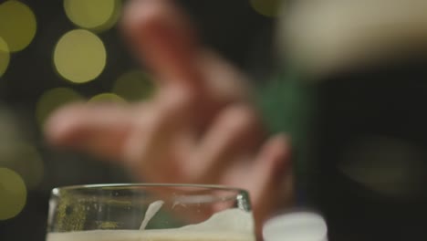 Close-Up-Of-Person-Talking-And-Drinking-Pint-Of-Irish-Stout-In-Pub-To-Celebrate-St-Patricks-Day