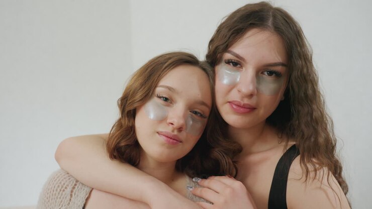 Casual Scene Of Two Sisters Enjoying Skincare, Warm Sisters Sharing Peaceful Beauty Routine Together Indoors, Closeup Of Two Women Relaxing With Eye Patches And Gentle Smiles In Cozy Setting