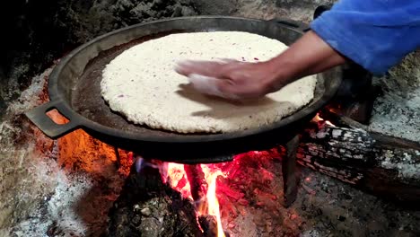 Primer-Plano-De-Cocinar-Pan-En-Una-Sartén-De-Hierro-Fundido-Descansando-Sobre-Salvamanteles,-Sobre-Un-Fuego-De-Madera-De-Roble-En-Una-Gran-Chimenea-De-Piedra-En-Una-Cocina-Tradicional-2