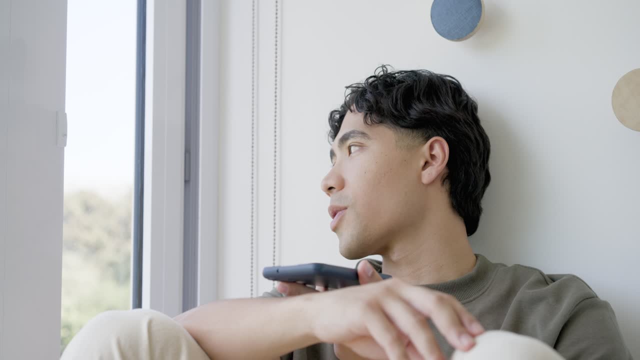 窓際の席に寄りかかって目を開け、外を見ているアジア人男性が、スマートフォンを上げてメッセージをタップしている。