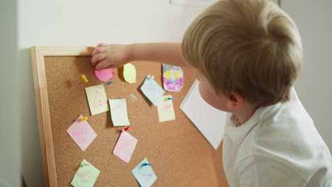 niño pequeño presiona figura de papel rosa a tablero de corcho