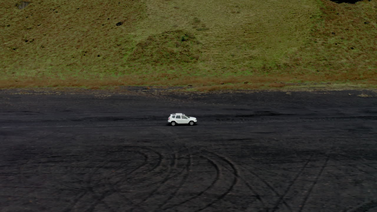항공:아이슬란드의 녹색 이끼 근처 검은 모래 해변에서 운전하는 흰색 자동차의 옆면