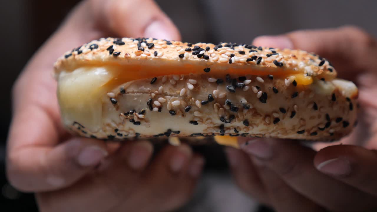 Primo piano di mani che tengono un delizioso bagel con formaggio fuso